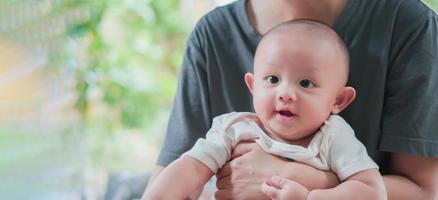 Authentic shot of Cute Asian newborn baby boy smile happy face while sitting with mother. Mom using hand take care, hug with love. Innocent little new infant adorable. Parenthood, mother day concept.