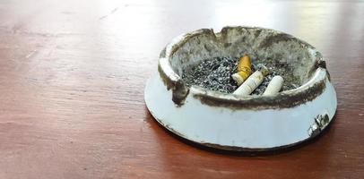 colillas de cigarrillos con cenizas en el fondo de la mesa de madera del cenicero foto