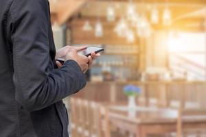 primer plano de un joven hombre de negocios que usa un teléfono inteligente móvil con un fondo borroso de cafetería foto