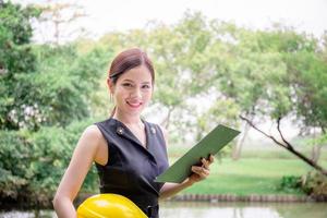 Young woman holding hardhat and clipboard checklist and looking at camera, Quality control concept photo