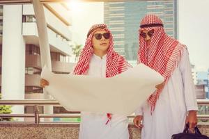 Young Arab Middle Eastern Business man team holding construction blueprints in hand against city background planing and management concepts photo