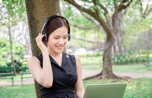Beautiful young woman with headphones and laptop enjoys and relaxed in music in the park