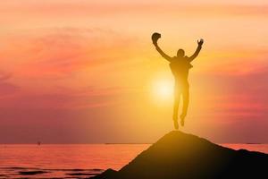 silueta de hombre de negocios celebración éxito felicidad en la cima de una montaña puesta de sol cielo de fondo, deporte y concepto de vida activa. foto