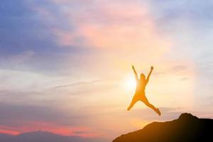 silueta de mujer feliz celebración éxito felicidad en la cima de una montaña puesta de sol cielo de fondo, deporte y concepto de vida activa. foto