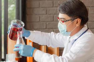 Doctor analyzing medical test tubes examining beaker with red fluid in laboratory
