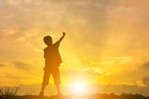 silueta del niño celebración éxito felicidad en la cima de una montaña cielo nocturno puesta de sol fondo, deporte y concepto de vida activa. foto