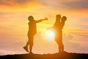 Silhouettes of mother daughter and son playing at sunset evening sky background photo