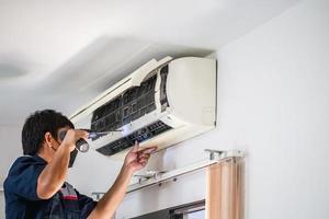 Male technician using a screwdriver fixing modern air conditioner, Male technician cleaning air conditioner indoors, Maintenance and repairing concepts photo