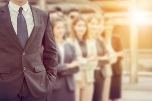 Close up of businessman standing with hands in pocket over blurry success business people team background photo