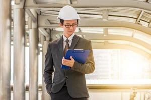 Business engineer planing with white helmet and holding drawing paper in hand against city background photo