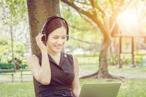 Beautiful young woman with headphones and laptop enjoys and relaxed in music in the park photo