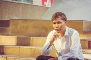 Alone business man thinking and sitting outside office blurry city background photo