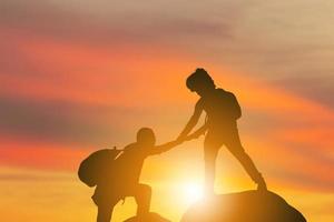 Silhouette of climbers man gived hand for pull hikers team to peak of mountain for work together, Sport and Teamwork Concept photo