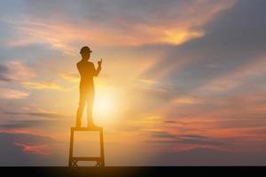 silueta de hombre de negocios celebración éxito felicidad en la cima de una montaña puesta de sol cielo de fondo, deporte y concepto de vida activa foto