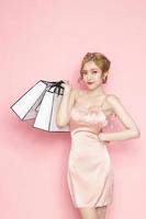 Retrato de una alegre y joven mujer asiática con piel limpia y fresca sosteniendo bolsas de compras con fondo rosa. consumismo, concepto de estilo de vida. foto