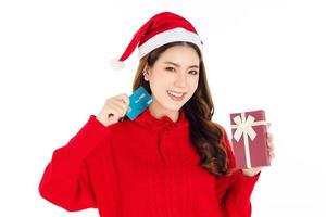 A cute Asian woman wearing a red dress with a Santa hat is holding a gift box. shopping concept. photo