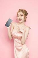 retrato alegre bastante joven mujer asiática emocionada sosteniendo el teléfono inteligente en su mano sobre fondo rosa. gran oferta móvil, consumismo, concepto de estilo de vida. foto