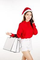 A cute Asian woman wearing a red dress with a Santa hat is holding a gift box. shopping concept. photo