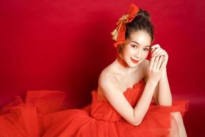 Young Asian pretty woman model in a posh stylish luxury red dress on a red background isolated. photo