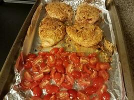 baking tray with sliced red tomatoes and chicken photo