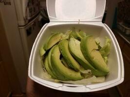 mano sujetando rodajas de aguacate verde con lechuga en un recipiente de espuma foto