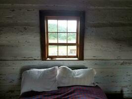cama con dos almohadas y ventana al exterior foto