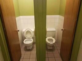 two toilets with stalls in green and white bathroom photo