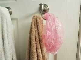 white and brown towel on hook on bathroom door with pink showercap photo