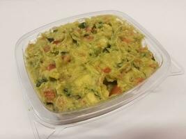 plastic container with avocado or guacamole on white surface photo