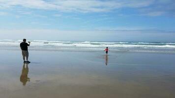 padre tomando una foto de su hijo en la arena y el agua en la playa