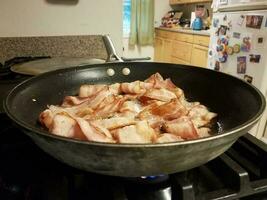 bacon cooking in frying pan or skillet on stove in kitchen photo