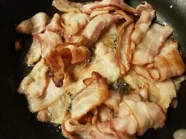 bacon cooking in frying pan or skillet on stove photo