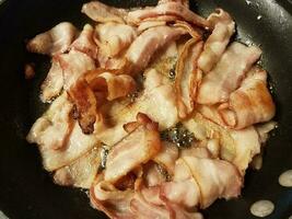 bacon cooking in frying pan or skillet on stove photo