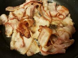 bacon cooking in frying pan or skillet on stove photo