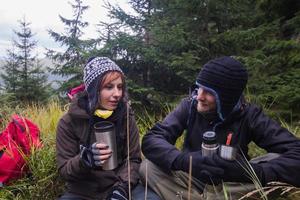 Young couple hikers with thermos cups in forest, travelers in mauntains drinking tea or coffee photo
