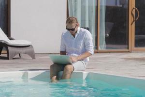 young men with laptopp working near the pool, freelancer in hotel on vacation with notebook photo