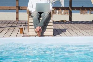young men with laptopp working near the pool, freelancer in hotel on vacation with notebook photo
