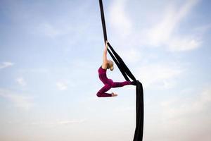 exercises with aerial silk outdoor, sky background. beautiful fit woman training acrobatic in airt. photo