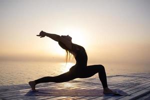 young woman posing in yoga asans, morning sea background photo