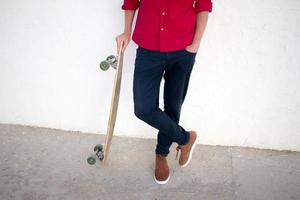 joven barbudo montando en patineta, hipster con longboard en camisa roja y blue jeans de fondo urbano foto
