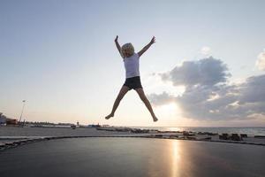 niña salta y se divierte en el trampolín en verano foto