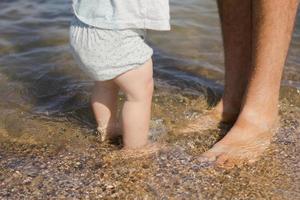 Close up picture of father with one year kid walking on the beach at summertime photo