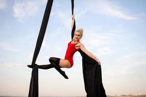 exercises with aerial silk outdoor, sky background. beautiful fit woman training acrobatic in airt. photo