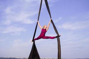 exercises with aerial silk outdoor, sky background. beautiful fit woman training acrobatic in airt. photo