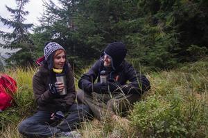 pareja joven excursionistas con tazas termos en el bosque, viajeros en mauntains bebiendo té o café foto