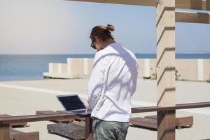 hombres jóvenes con laptop trabajando cerca de la piscina, freelancer en hotel de vacaciones con notebook foto