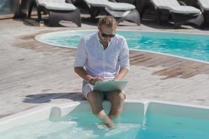 young men with laptopp working near the pool, freelancer in hotel on vacation with notebook photo