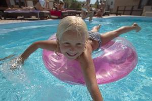 niño rubio pasándoselo bien en la piscina, niñita nadando en verano foto