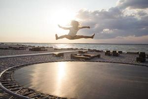 niña salta y se divierte en el trampolín en verano foto