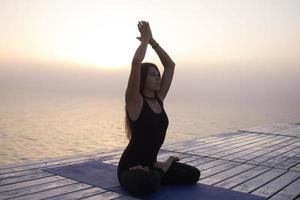 young woman posing in yoga asans, morning sea background photo